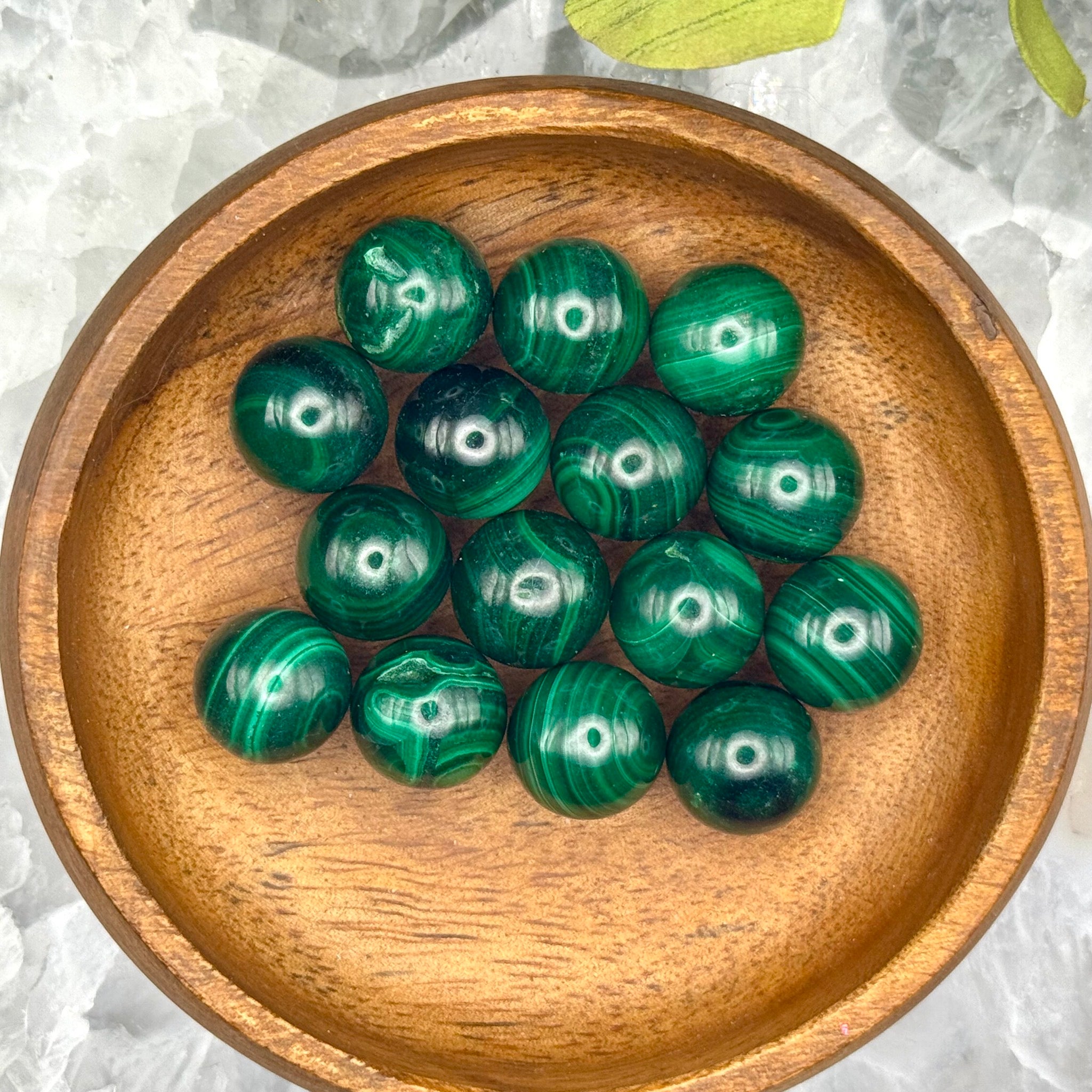 Green malachite spheres in a wooden bowl on an agate surface