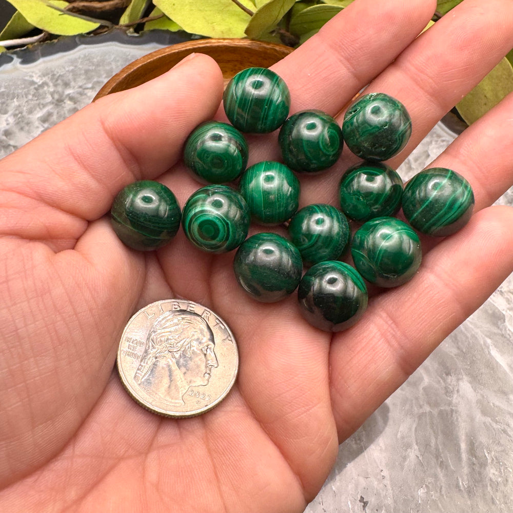 Green malachite spheres, on a hand with a quarter for size comparison.