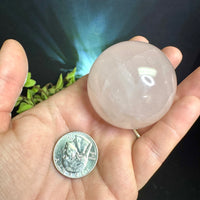 Hand holding a Rose Quartz crystal sphere next to a quarter for scale