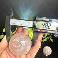Digital caliper measuring a Rose Quartz sphere held in a hand with a blurred background